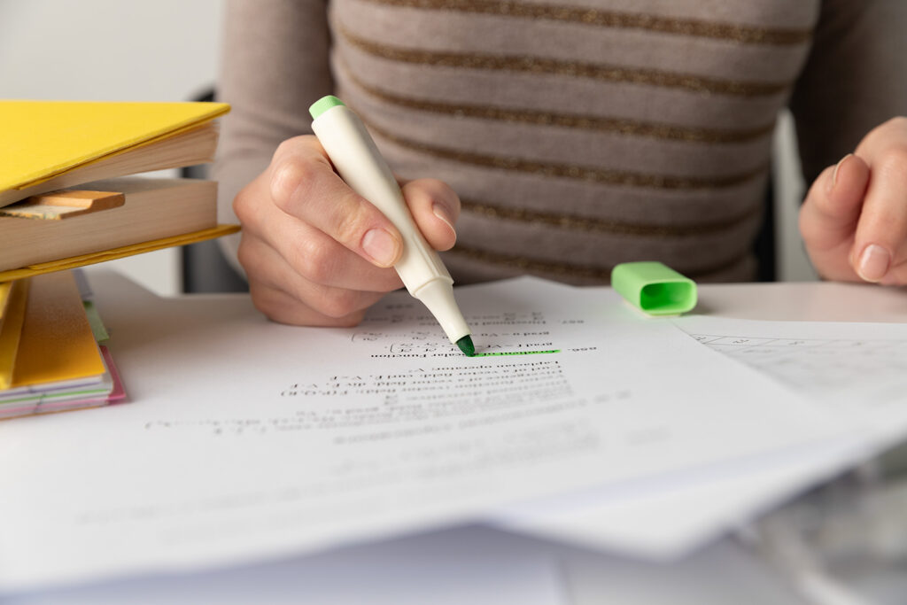 Close up of a person using a highlighter on a sheet of printed paper.